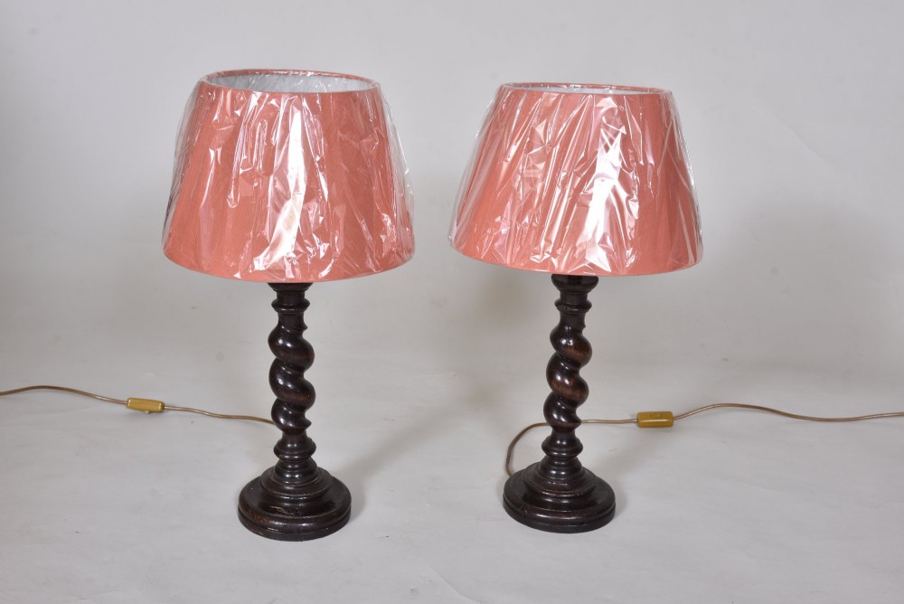 A pair of 19th-century dark oak table lamps featuring carved barley twist stems, circular bases, and terracotta-pink fabric lampshades.