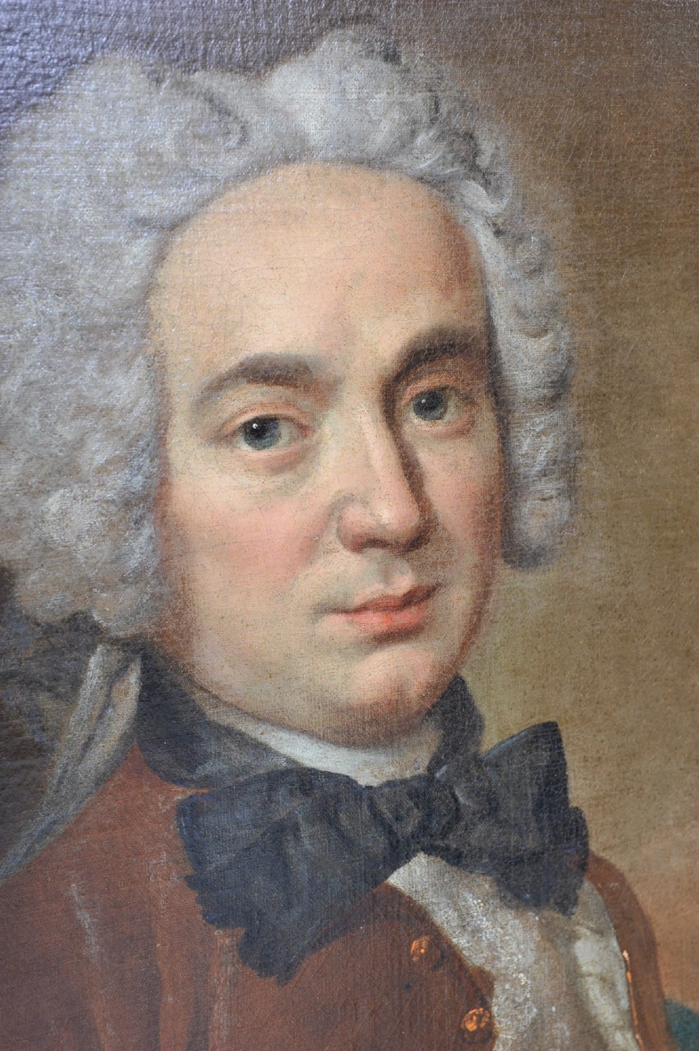 An eighteenth-century oil painting depicting a gentleman wearing a powdered wig, brown coat, black cravat, and blue drape, set within a carved gilt and dark wood frame. View IV