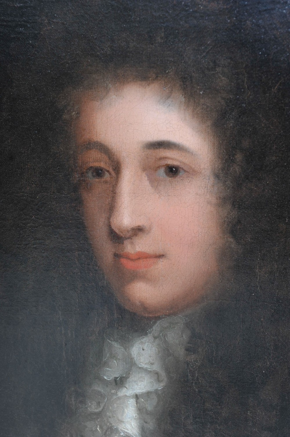 An oil painting depicting a 17th-century gentleman with a dark periwig and lace cravat set within an oval spandrel and a carved gilded frame. View II