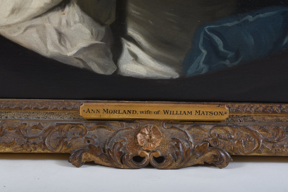 An 18th-century oil painting on canvas depicting a seated woman in a cream satin dress with a blue wrap, set within an ornate carved giltwood frame. View IV