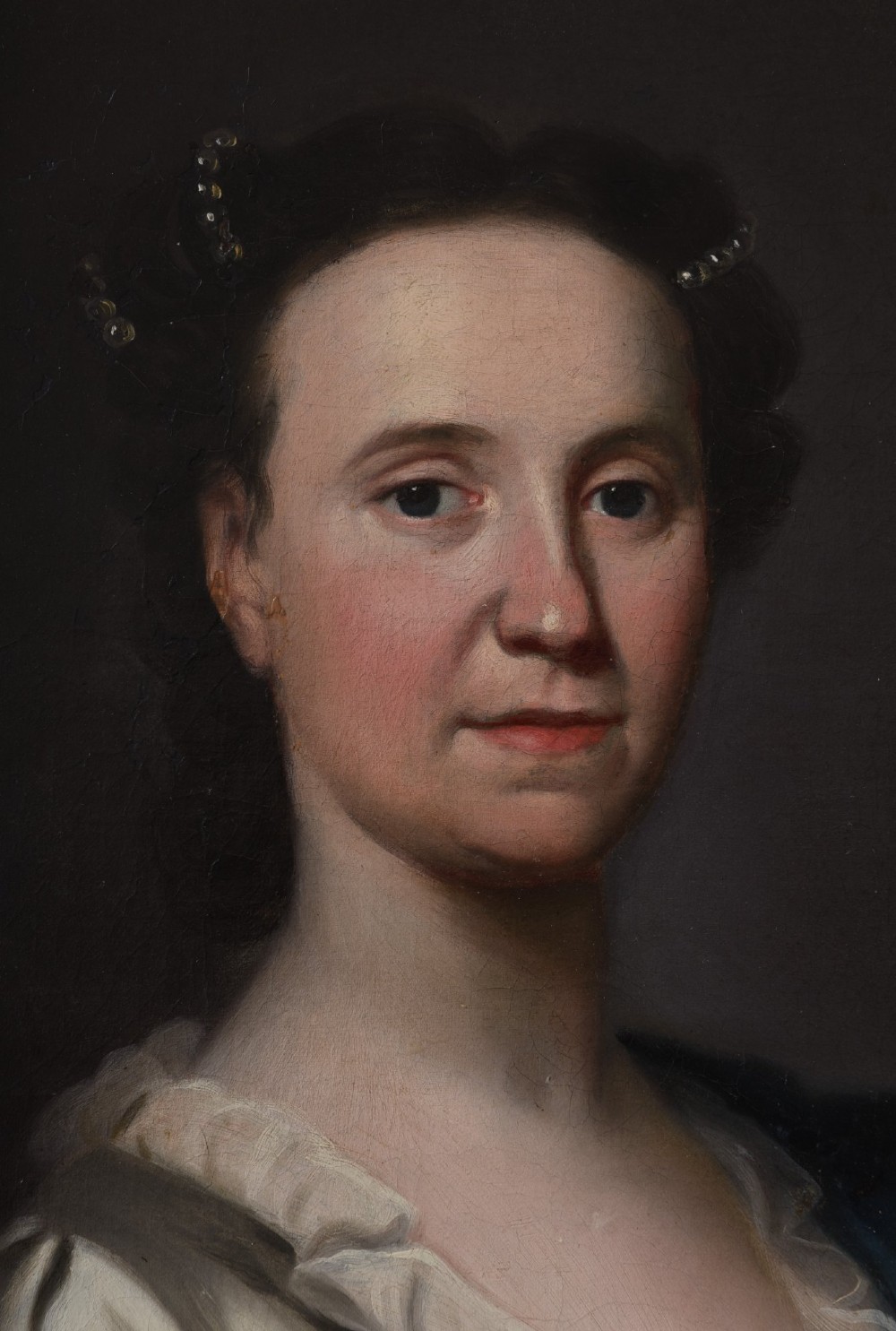 An 18th-century oil painting on canvas depicting a seated woman in a cream satin dress with a blue wrap, set within an ornate carved giltwood frame. View VI