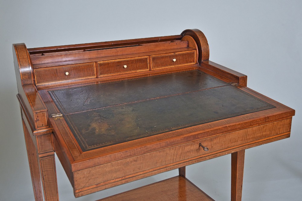 A 19th-century satinwood cylinder bureau featuring an inlaid curved roll-top hood, frieze drawer, square tapered legs, and a shaped lower shelf. View V