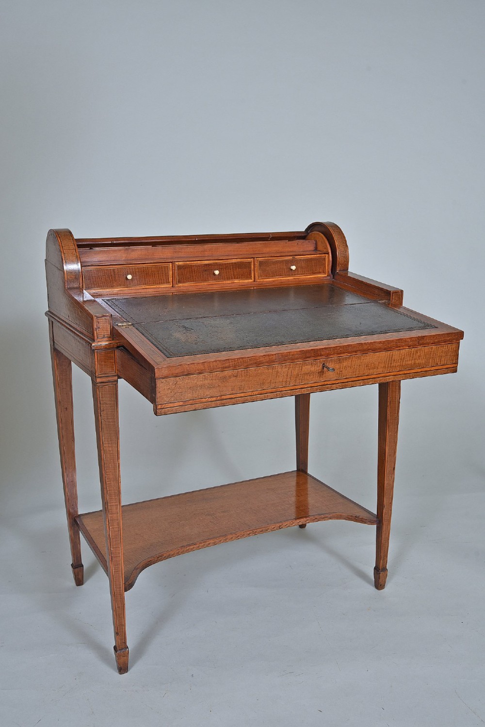 A 19th-century satinwood cylinder bureau featuring an inlaid curved roll-top hood, frieze drawer, square tapered legs, and a shaped lower shelf. View VI