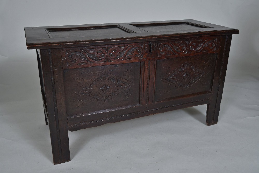 A dark 17th-century oak coffer featuring carved foliate friezes, panelled front with lozenge motifs, and a hinged lid.