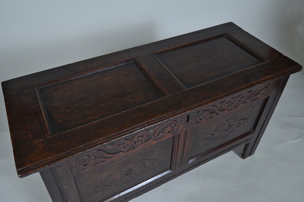 A dark 17th-century oak coffer featuring carved foliate friezes, panelled front with lozenge motifs, and a hinged lid. View III
