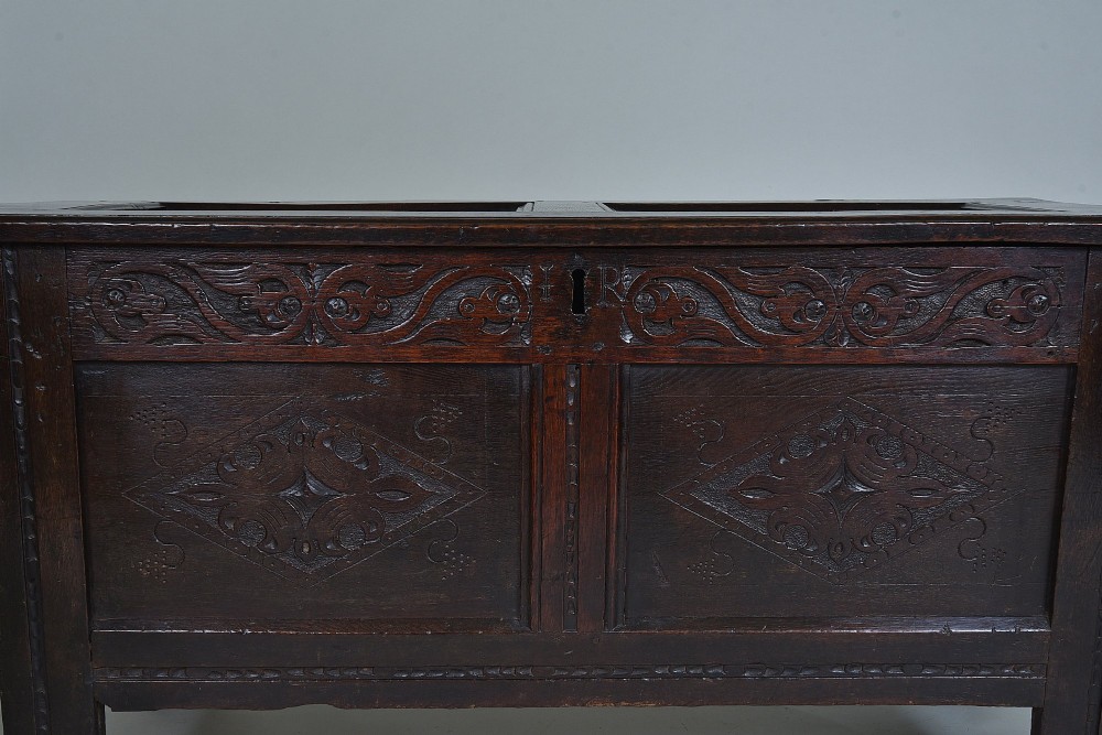 A dark 17th-century oak coffer featuring carved foliate friezes, panelled front with lozenge motifs, and a hinged lid. View IV
