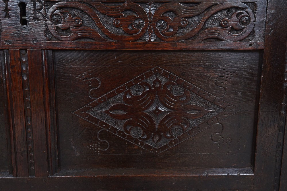 A dark 17th-century oak coffer featuring carved foliate friezes, panelled front with lozenge motifs, and a hinged lid. View V