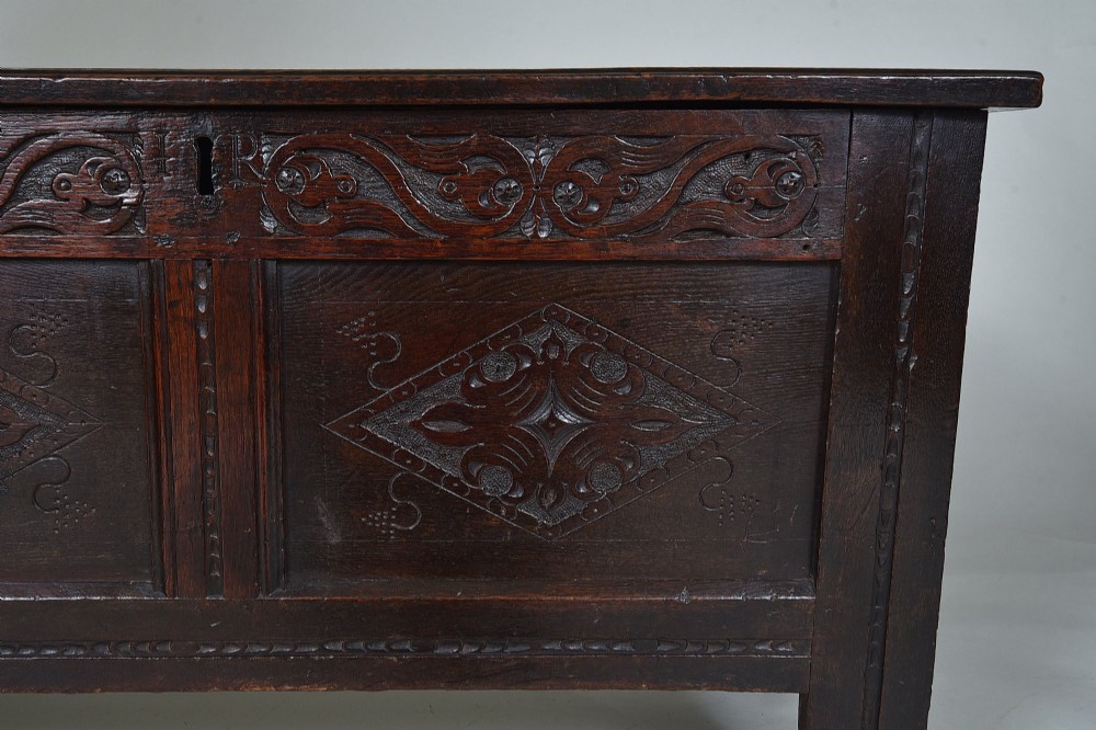 A dark 17th-century oak coffer featuring carved foliate friezes, panelled front with lozenge motifs, and a hinged lid. View VI