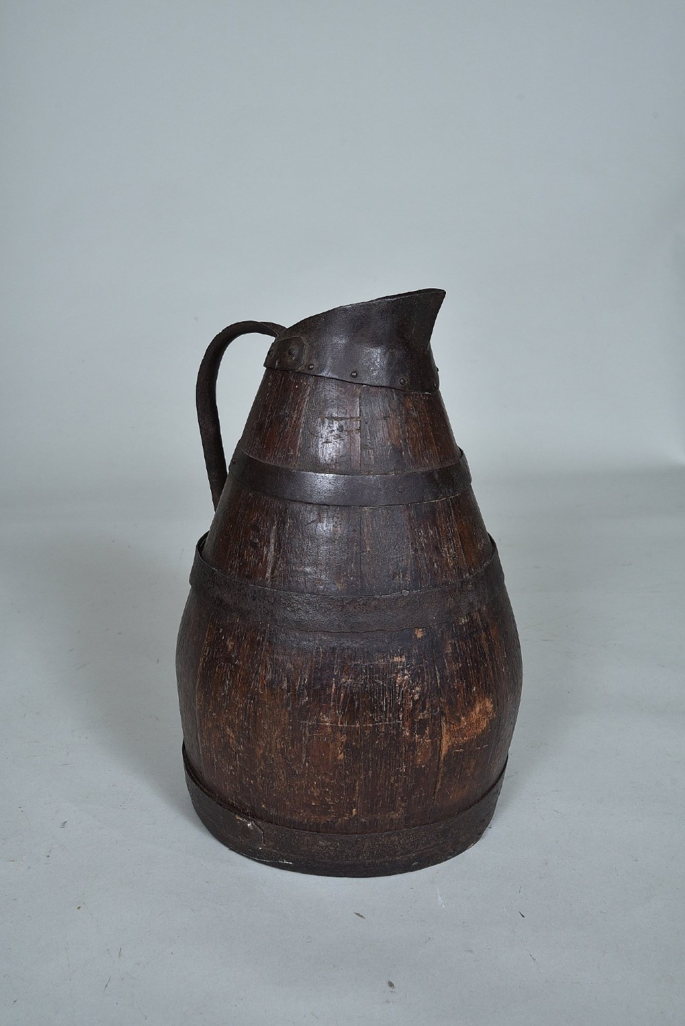 A dark brown 19th-century staved oak harvest jug featuring wrought iron bands, a pour spout, and a curved metal handle. View II
