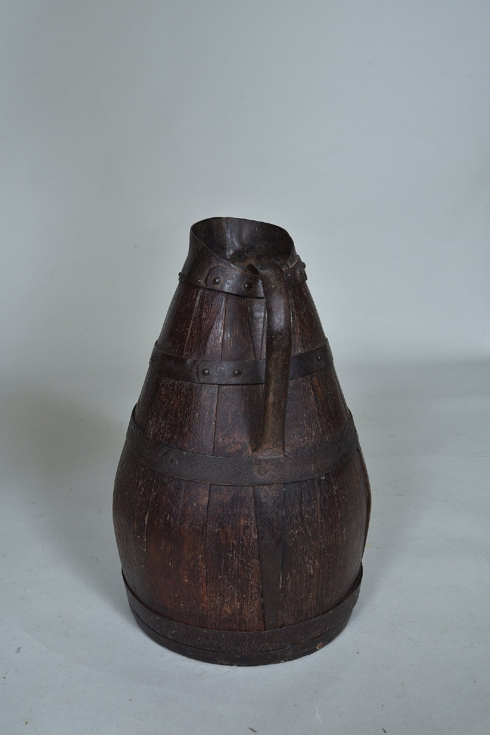 A dark brown 19th-century staved oak harvest jug featuring wrought iron bands, a pour spout, and a curved metal handle. View III