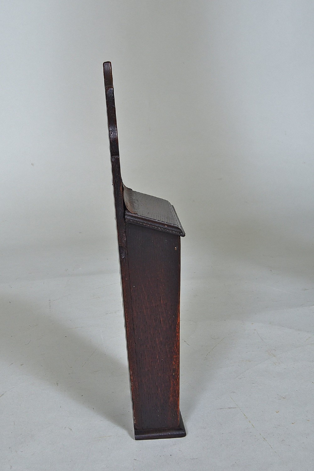 A dark oak wall-hanging candle box featuring a shaped backboard with a hanging aperture, a sliding front cover, and a tapered body. View III