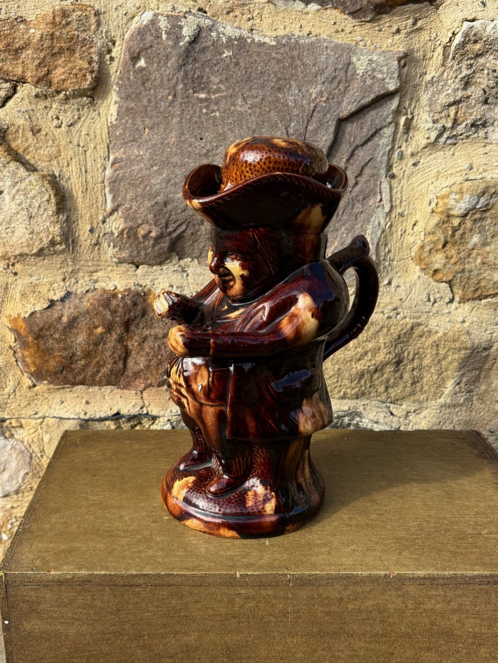 A nineteenth-century ceramic Toby jug depicting a seated man wearing a tricorne hat, finished in a rich, mottled treacle-brown glaze.