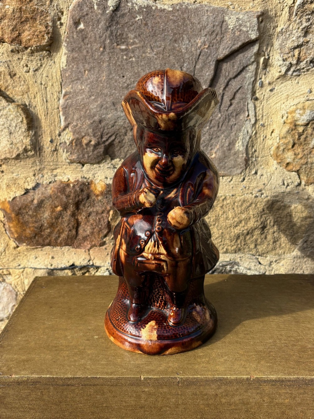 A nineteenth-century ceramic Toby jug depicting a seated man wearing a tricorne hat, finished in a rich, mottled treacle-brown glaze. View II