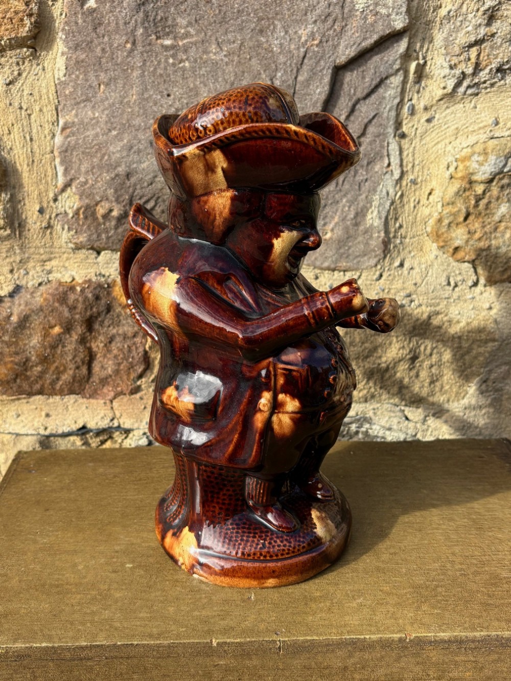 A nineteenth-century ceramic Toby jug depicting a seated man wearing a tricorne hat, finished in a rich, mottled treacle-brown glaze. View III