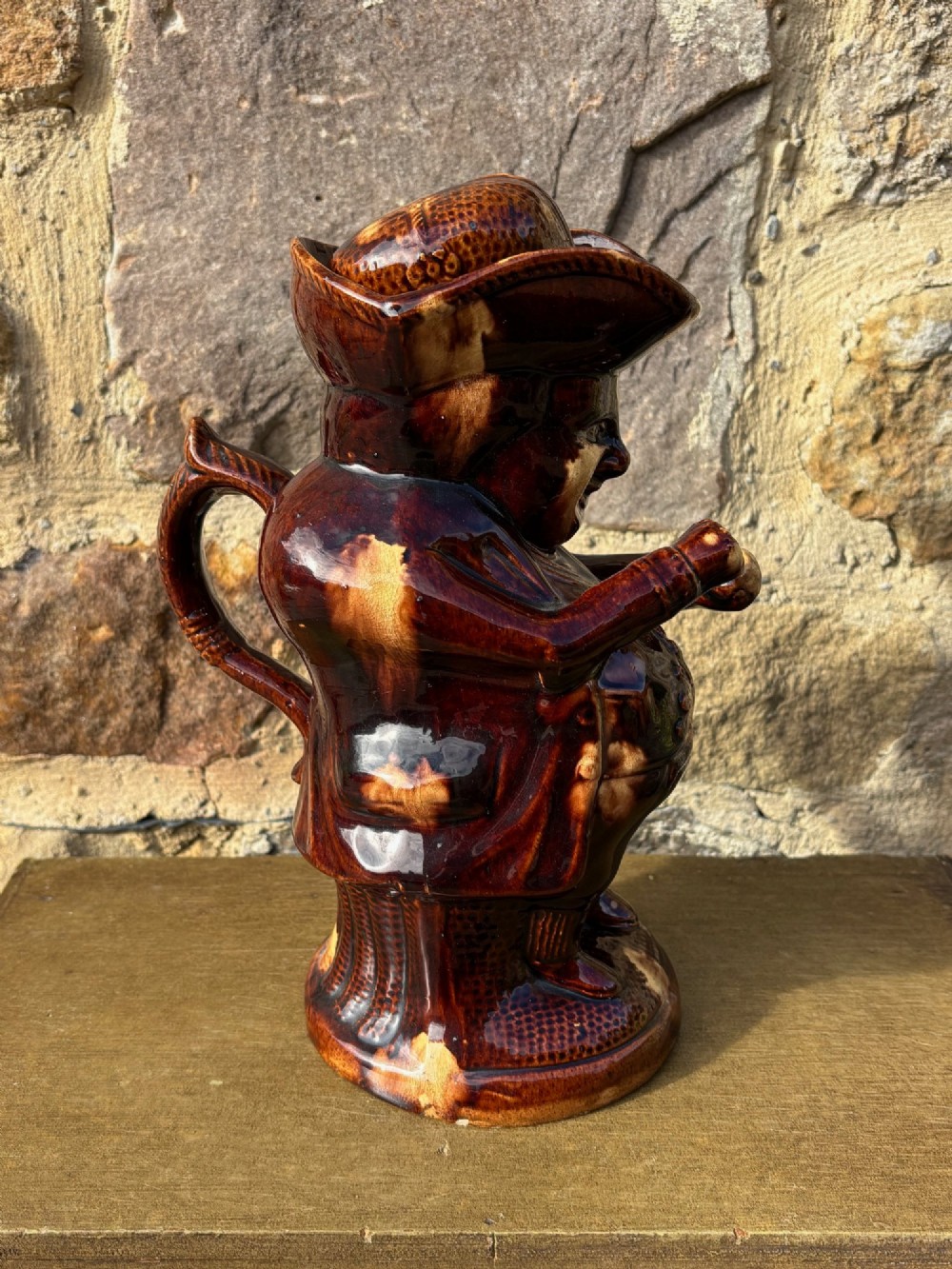 A nineteenth-century ceramic Toby jug depicting a seated man wearing a tricorne hat, finished in a rich, mottled treacle-brown glaze. View IV