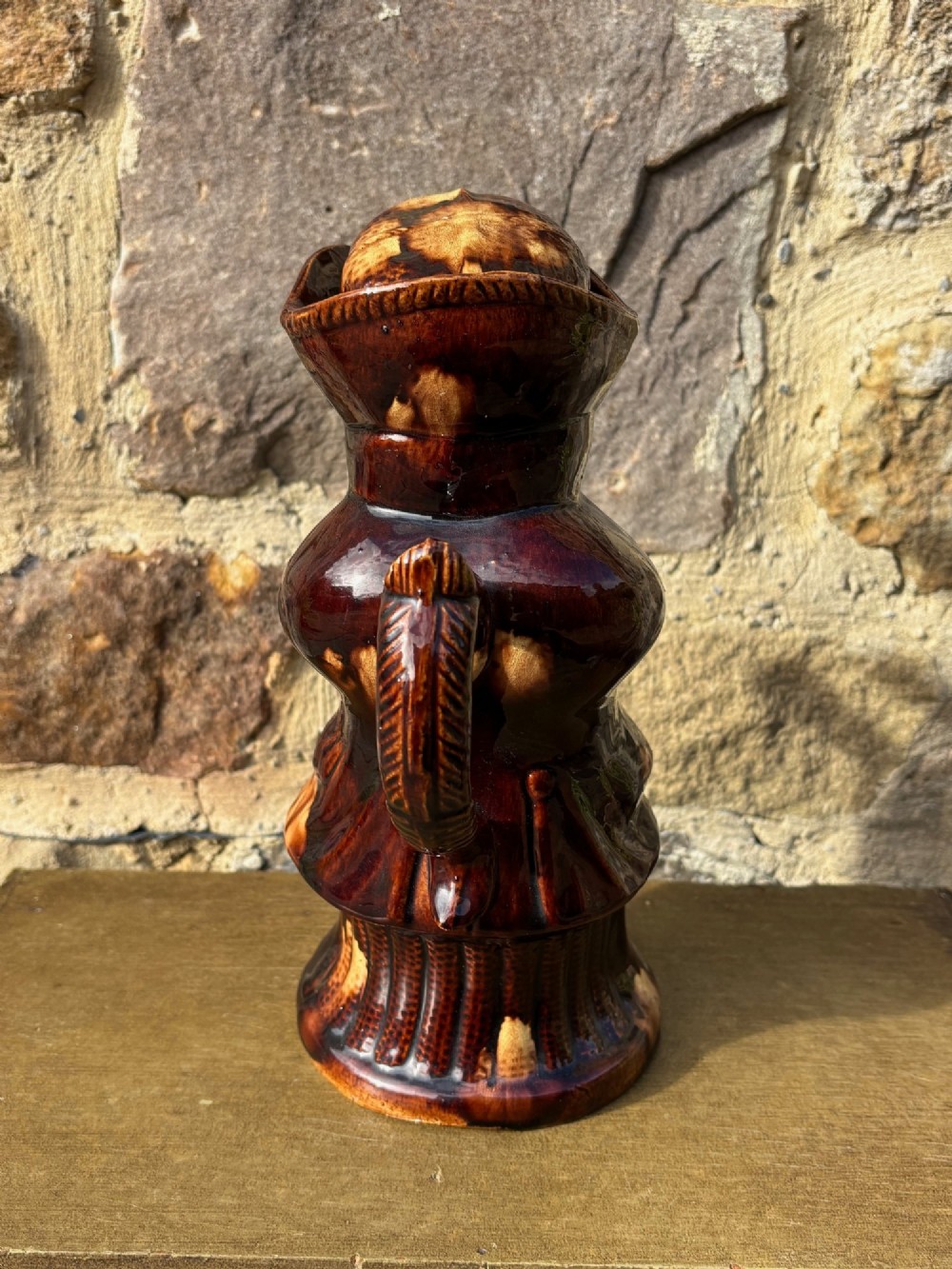 A nineteenth-century ceramic Toby jug depicting a seated man wearing a tricorne hat, finished in a rich, mottled treacle-brown glaze. View V