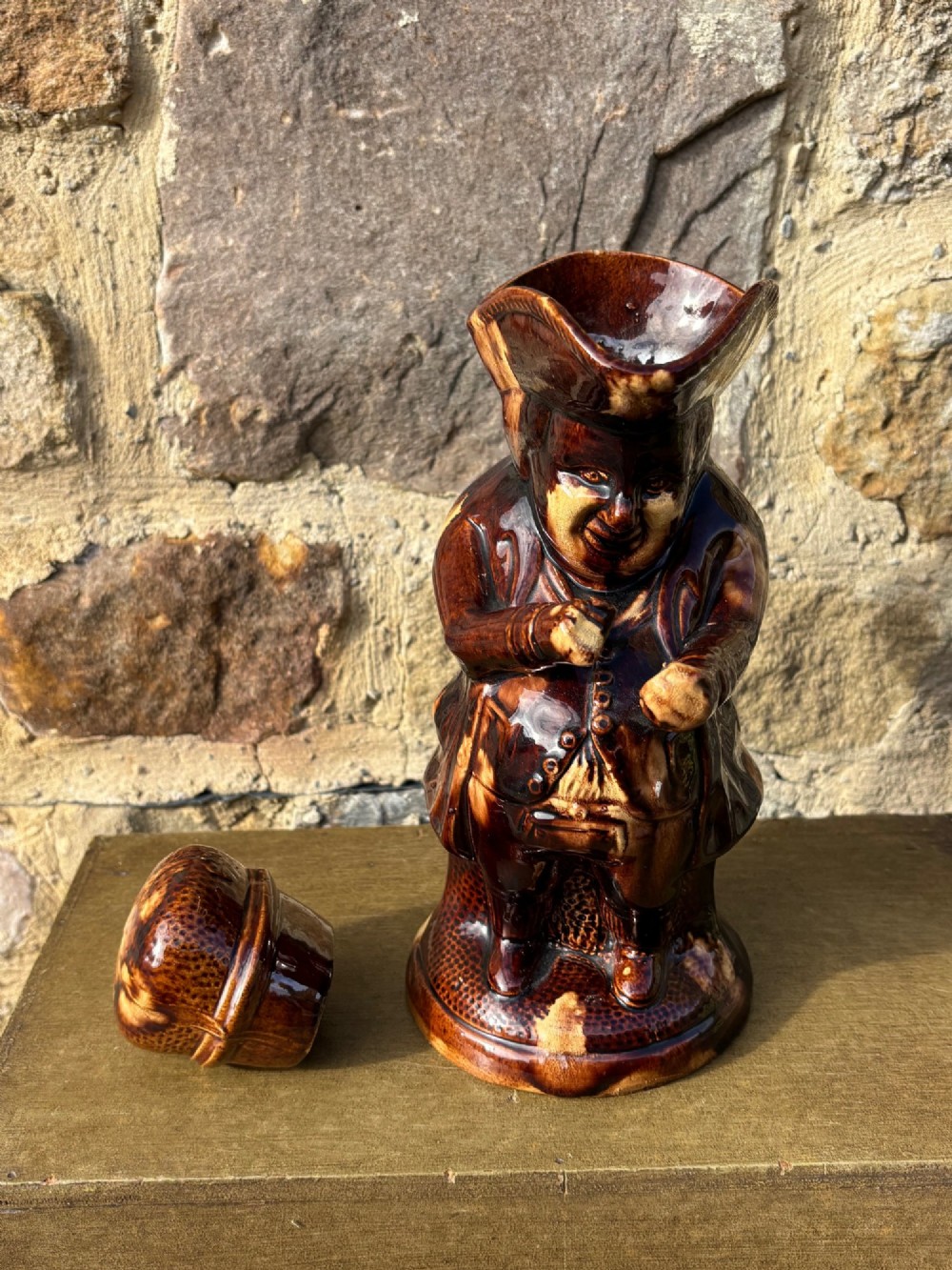 A nineteenth-century ceramic Toby jug depicting a seated man wearing a tricorne hat, finished in a rich, mottled treacle-brown glaze. View VII