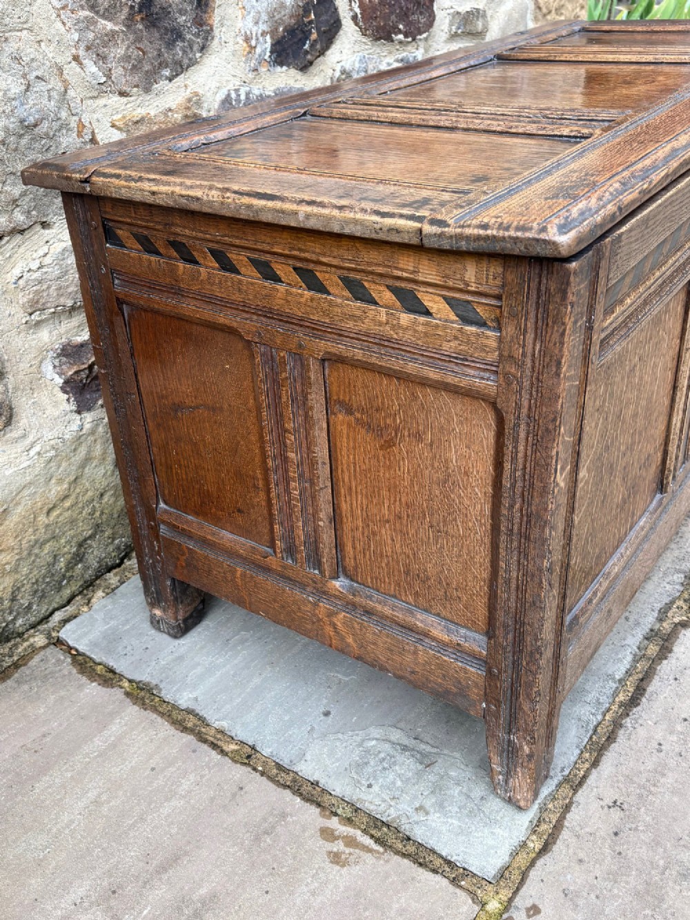 A 17th-century oak coffer featuring a hinged lid, panelled front, and geometric marquetry inlay. View V