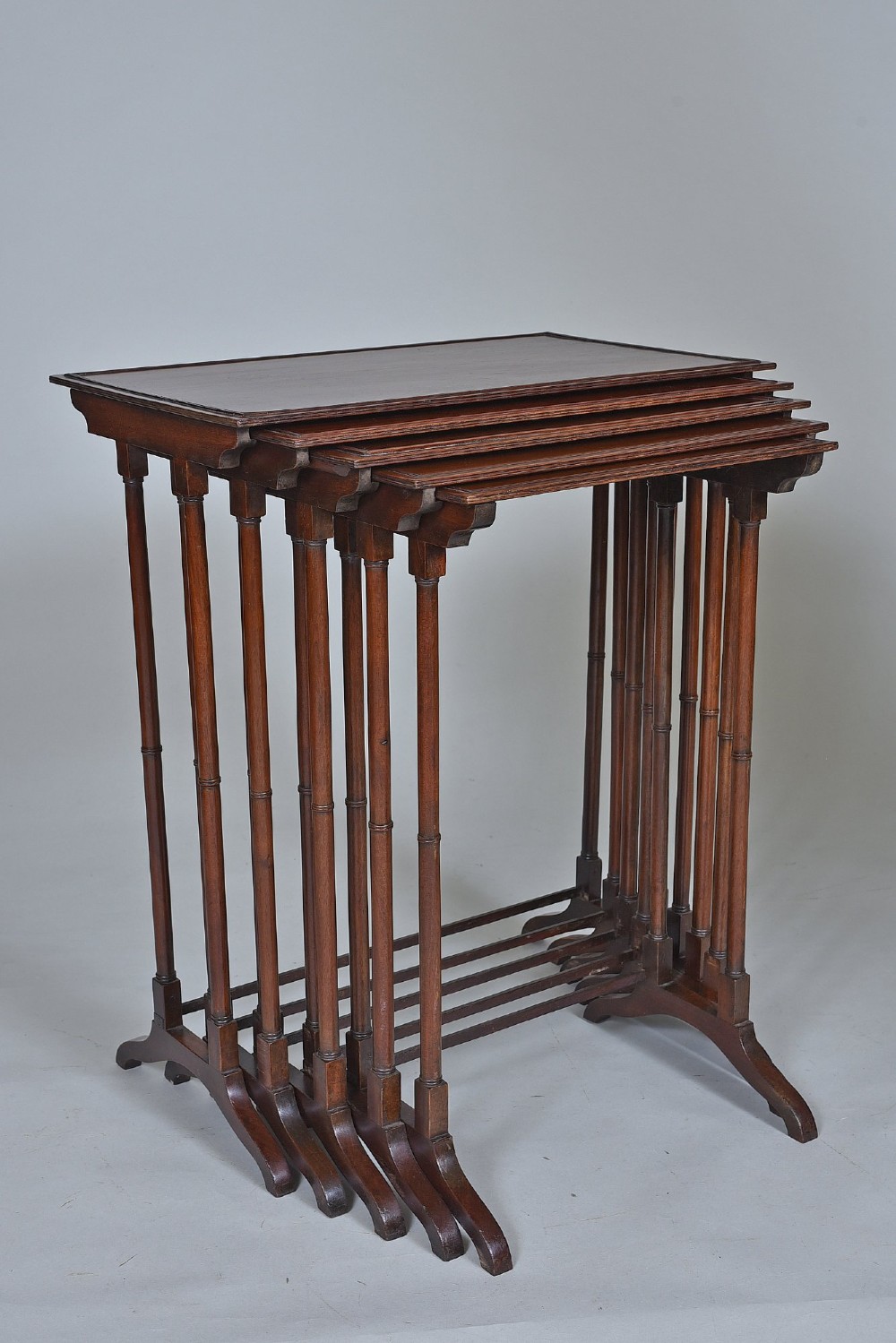 A set of five graduating antique mahogany nesting tables stacked together featuring slender turned legs and trestle feet.