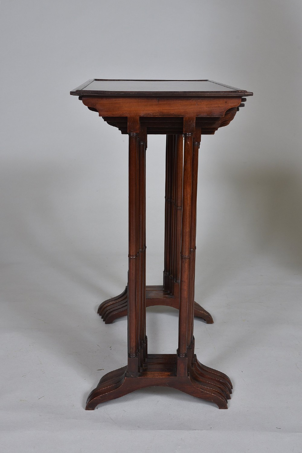 A set of five graduating antique mahogany nesting tables stacked together featuring slender turned legs and trestle feet. View IV