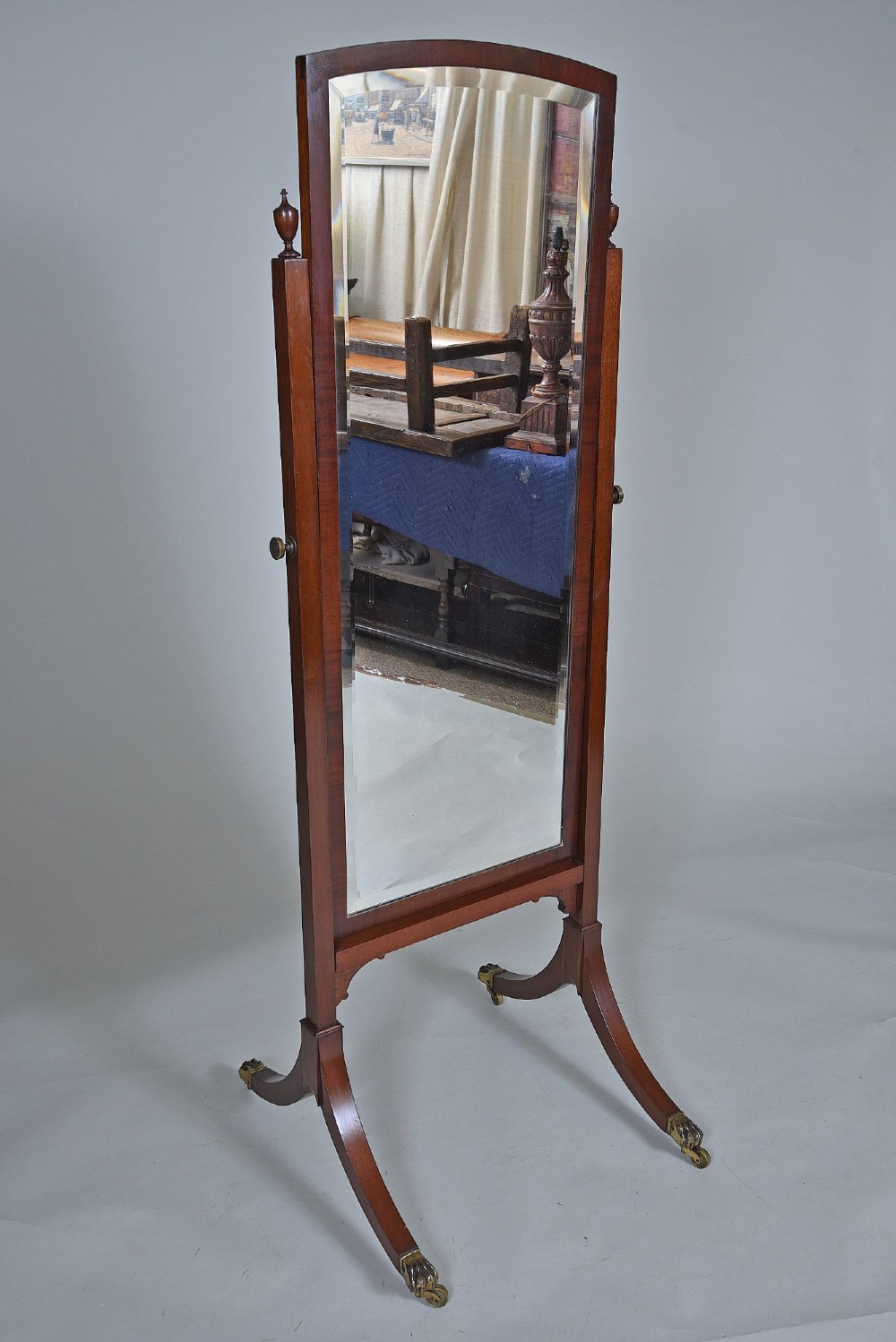 An Edwardian mahogany cheval mirror with an arched frame suspended on upright posts, raised on splayed legs with brass paw castors. View II