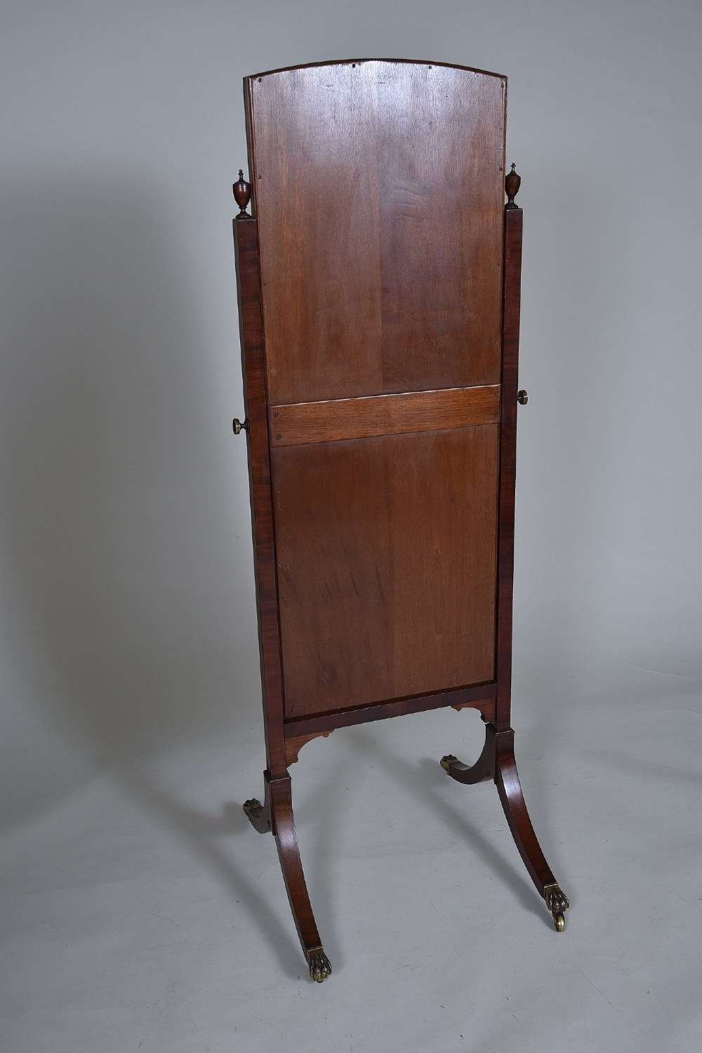 An Edwardian mahogany cheval mirror with an arched frame suspended on upright posts, raised on splayed legs with brass paw castors. View VI