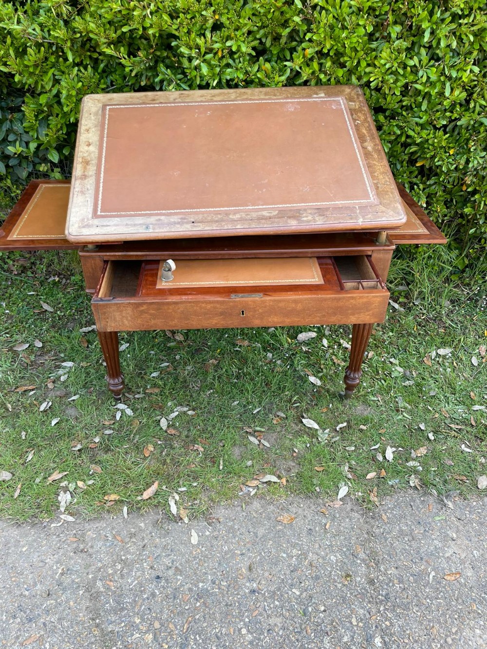 An antique mahogany William IV writing desk featuring a leather inset top, two pull-out side slides, a central drawer, and reeded turned legs on brass castors.