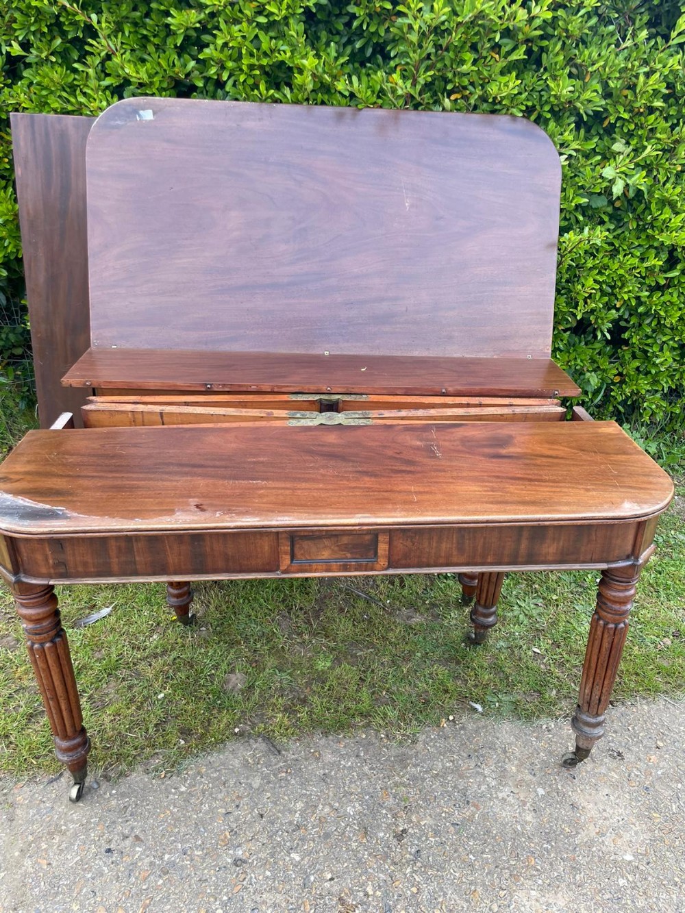 An antique mahogany extending dining table displaying an exposed wooden concertina mechanism, reeded legs on brass castors, and a detached top leaf.