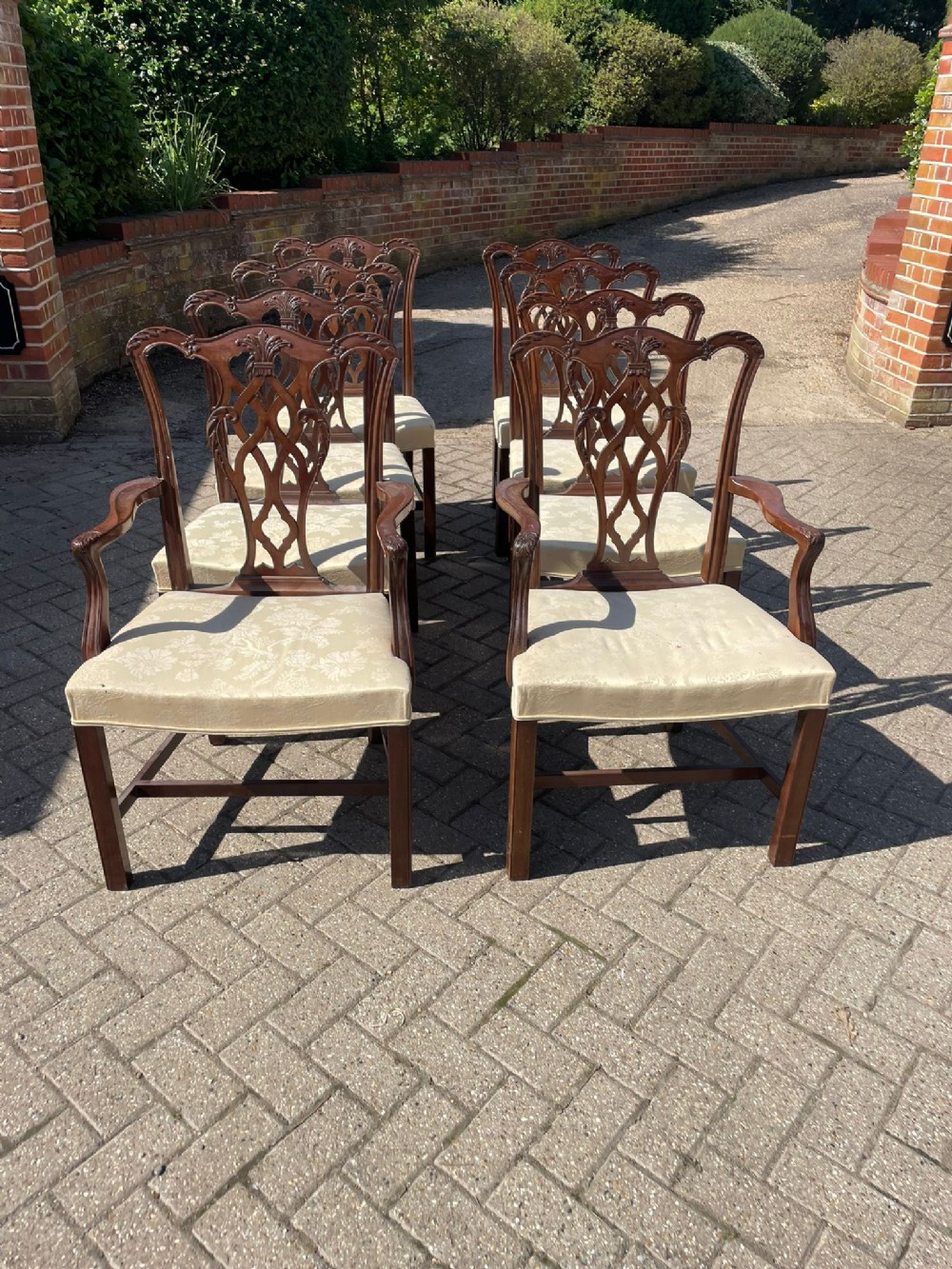 A set of eight antique Chippendale style mahogany dining chairs featuring carved pierced back splats and light cream upholstered seats.