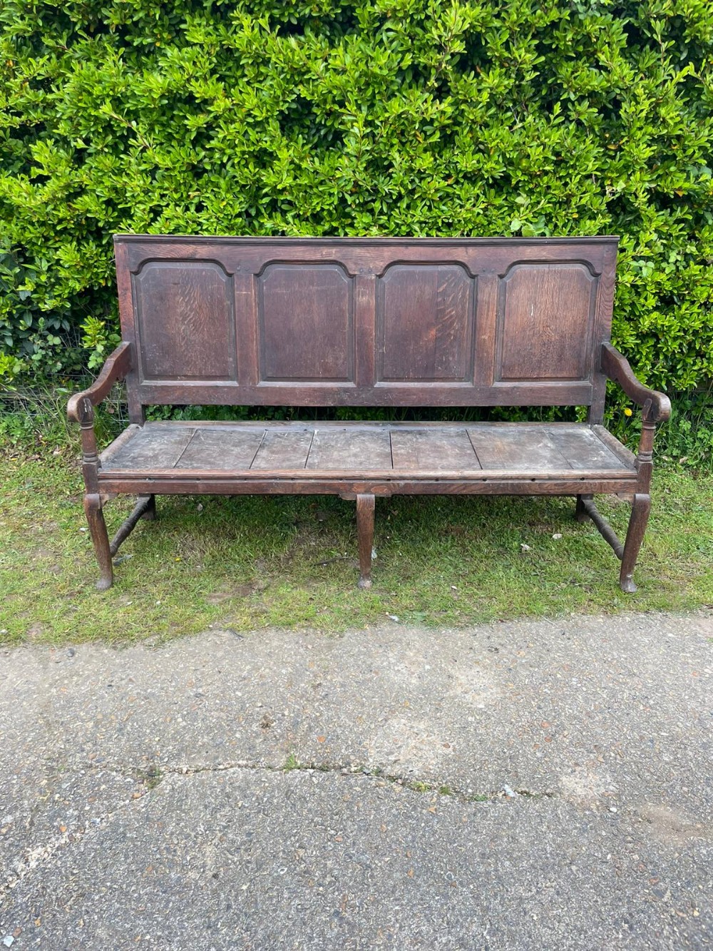 A George III dark oak settle featuring four fielded back panels, shaped armrests, and cabriole front legs.