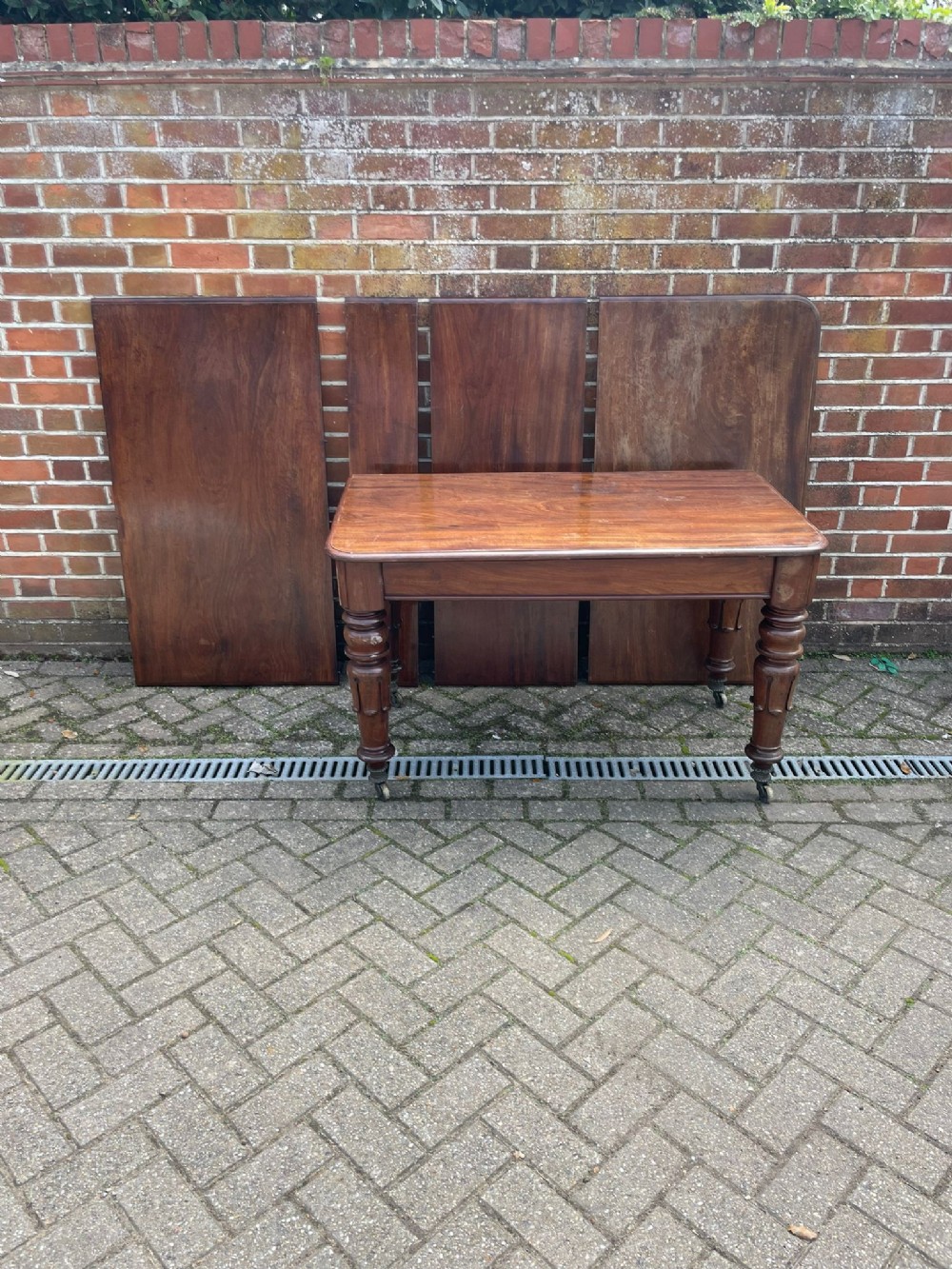 A William IV mahogany extending dining table with turned legs and brass castors, displayed with four loose leaves behind it.