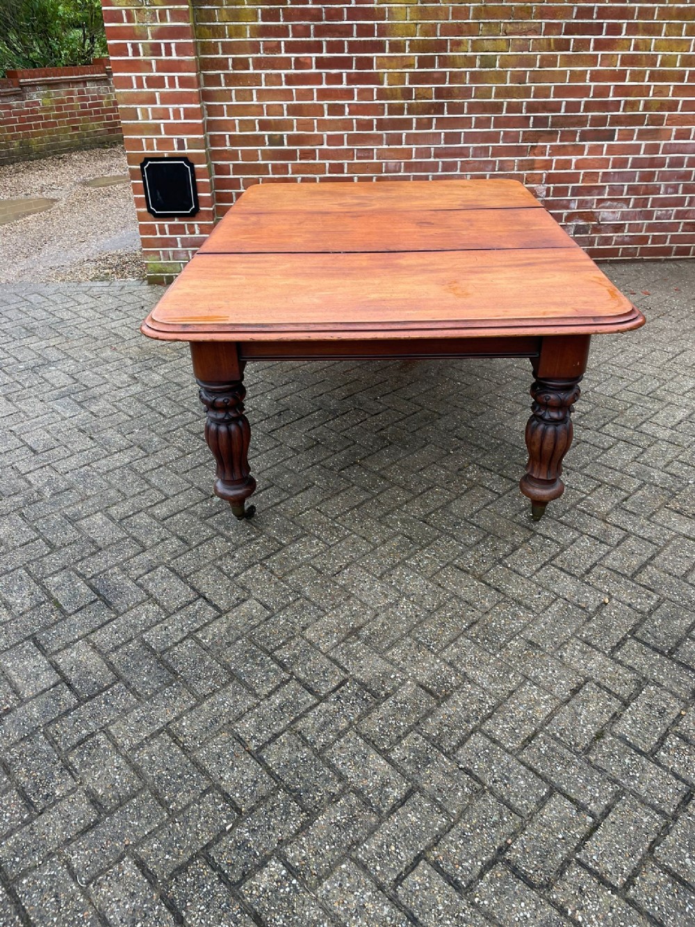 A large Victorian mahogany extending dining table with rounded corners, heavy turned carved legs, and brass castors.