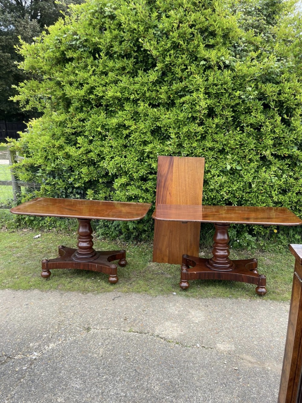 An antique mahogany twin pedestal dining table featuring turned central columns, shaped platform bases, spherical feet, and a removable extension leaf.