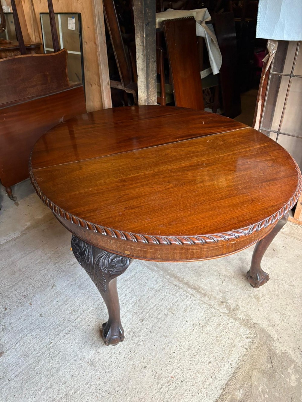 A circular antique mahogany dining table featuring carved cabriole legs with acanthus knee details, ball-and-claw feet, and a carved rope-twist edge.