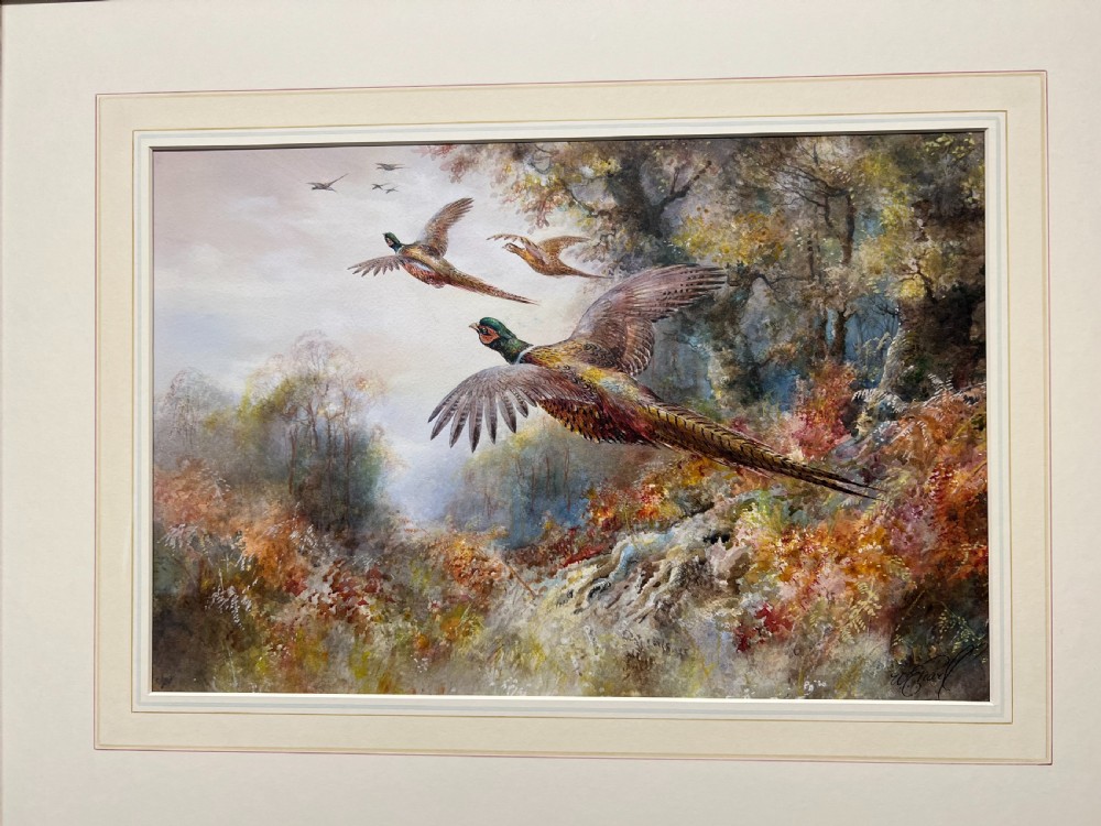 A framed watercolour painting depicting pheasants in flight above an autumnal woodland landscape.