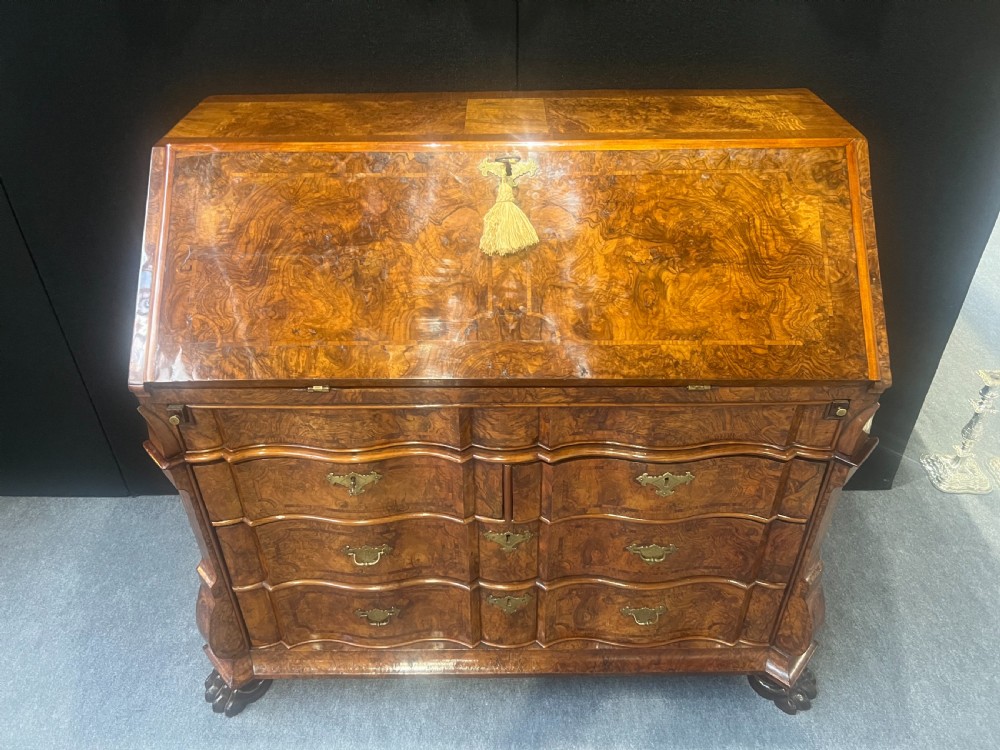 An antique burr walnut slant-front writing bureau featuring serpentine front drawers, brass escutcheons, and carved feet.