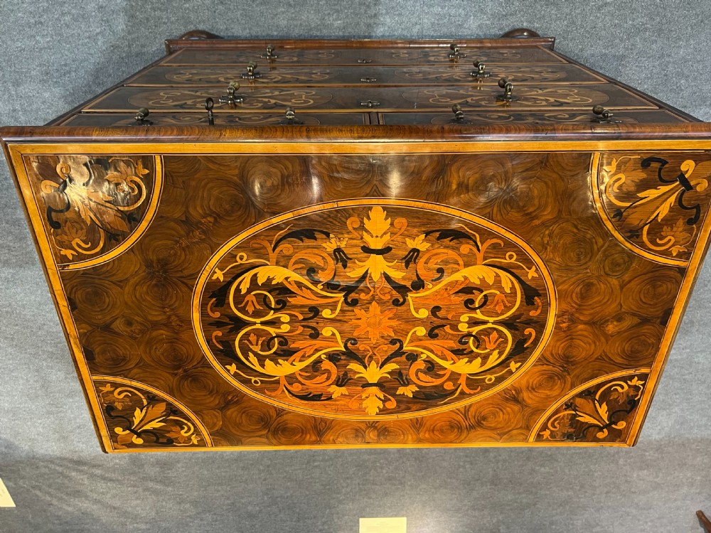 A walnut chest of drawers featuring intricate floral marquetry inlay across the drawer fronts and top surface, fitted with brass drop handles and raised on bun feet. View II
