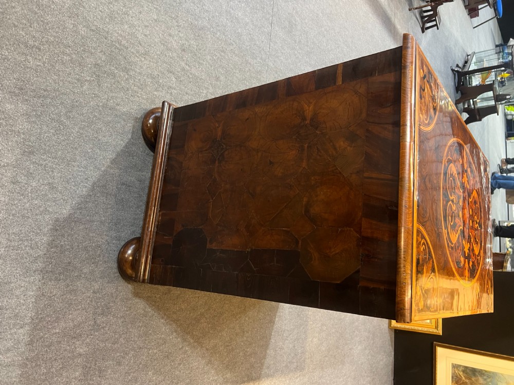 A walnut chest of drawers featuring intricate floral marquetry inlay across the drawer fronts and top surface, fitted with brass drop handles and raised on bun feet. View III