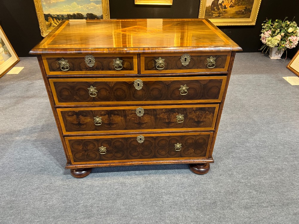 An antique burr walnut chest of drawers featuring inlaid geometric patterns on top, two short over three long drawers with brass handles, and bun feet.