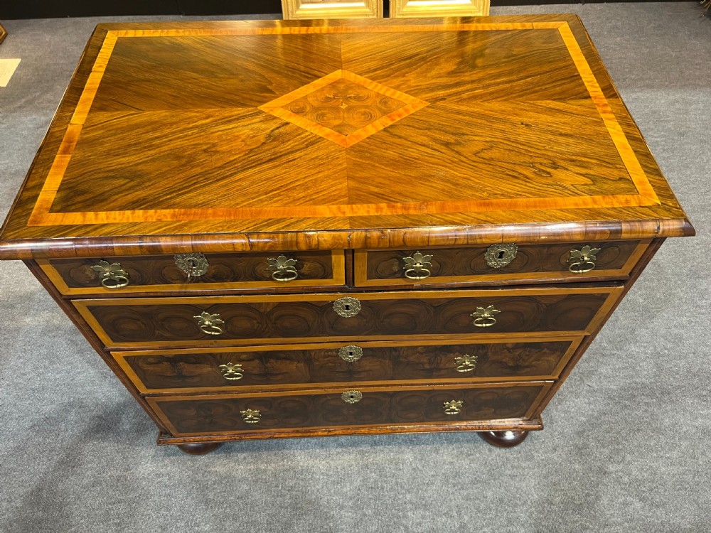 An antique burr walnut chest of drawers featuring inlaid geometric patterns on top, two short over three long drawers with brass handles, and bun feet. View II
