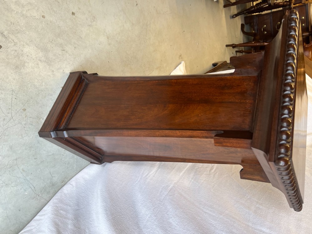 A tall dark mahogany pedestal stand featuring carved egg-and-dart moulding around the top edge, a tapered central shaft, and a stepped rectangular base. View II