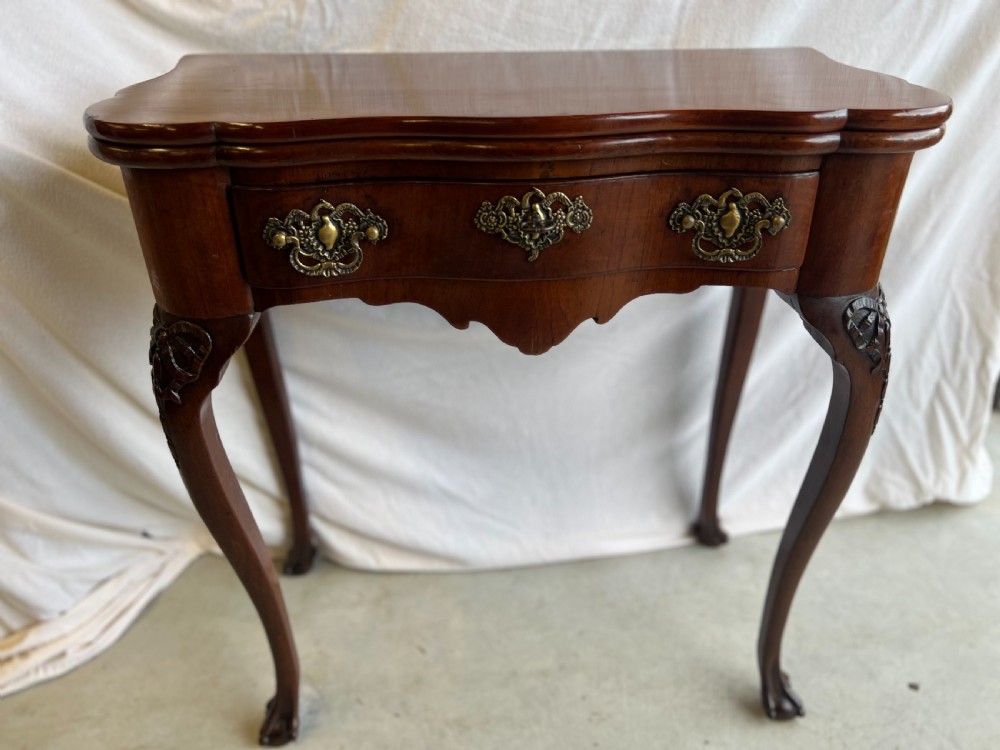 A mahogany fold-over tea table featuring a serpentine front, ornate brass bail handles, a shaped apron, and carved cabriole legs.
