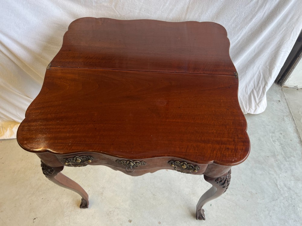 A mahogany fold-over tea table featuring a serpentine front, ornate brass bail handles, a shaped apron, and carved cabriole legs. View V