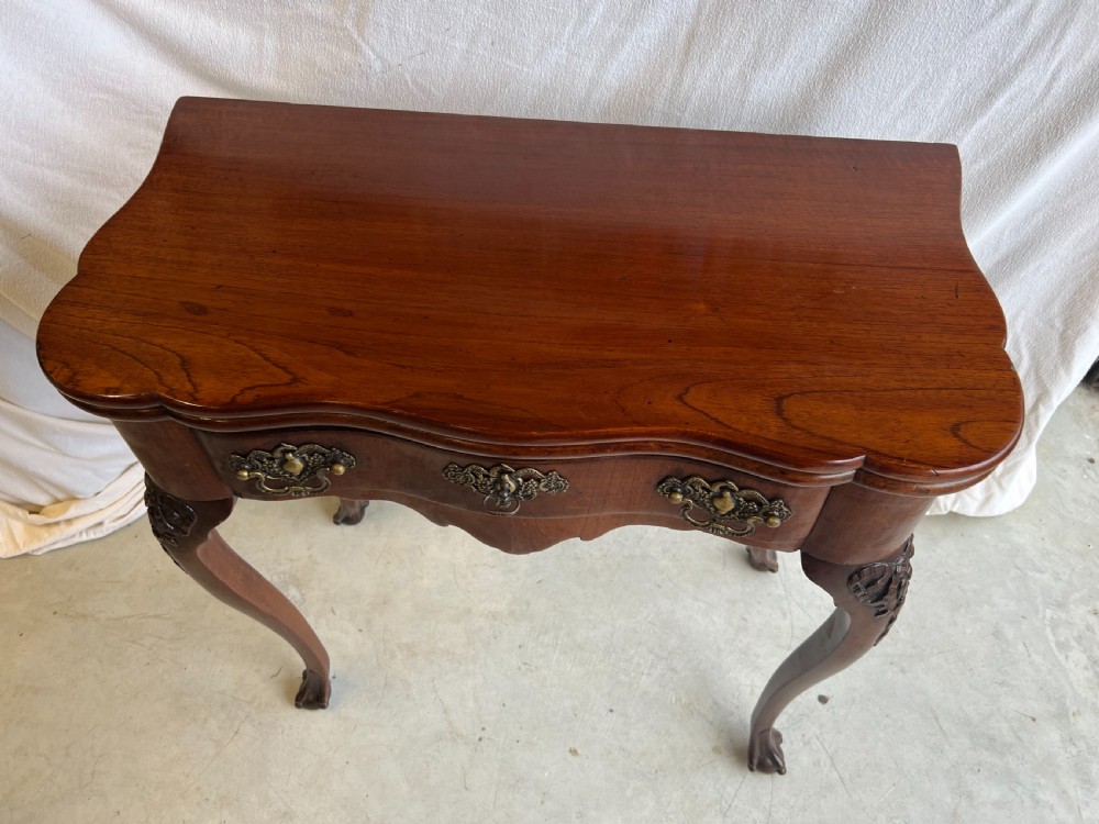 A mahogany fold-over tea table featuring a serpentine front, ornate brass bail handles, a shaped apron, and carved cabriole legs. View VI