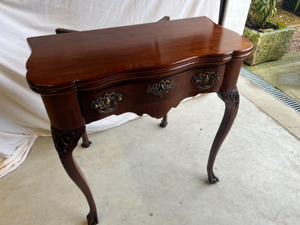 A mahogany fold-over tea table featuring a serpentine front, ornate brass bail handles, a shaped apron, and carved cabriole legs. View VII