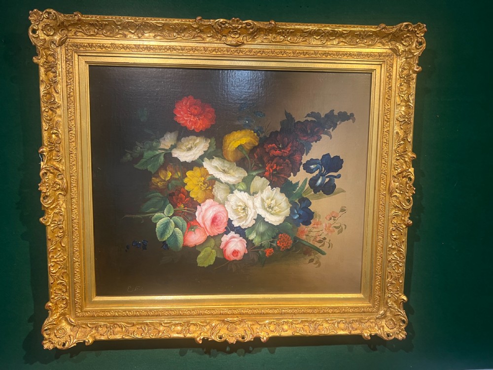 A Victorian floral oil painting depicting an arrangement of colourful roses, irises, and dahlias inside a carved gilded frame against a dark backdrop.