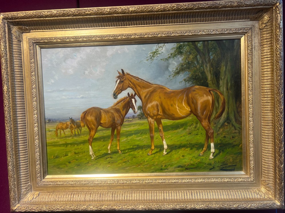 An antique oil painting depicting a chestnut mare and foal standing in a green field, presented in an ornate gilded frame.
