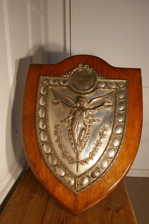fig 1. A shield-shaped oak wall plaque featuring a silver-plated relief of the winged goddess Nike surrounded by laurel motifs and small engraved oval shields.