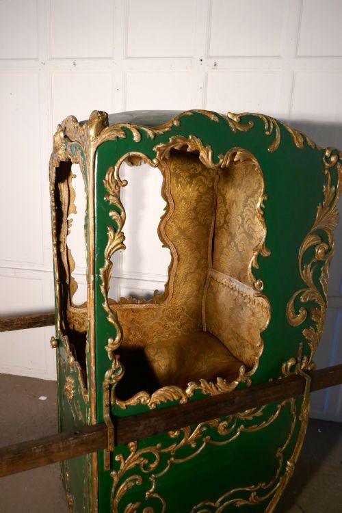 fig 1. A 19th-century green painted and giltwood Italian sedan chair featuring hand-carved scrollwork, window openings, gold fabric lining, and wooden carrying poles.