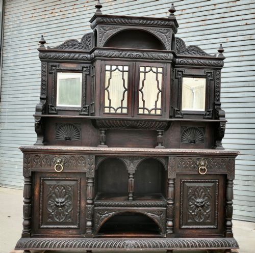 fig 1. A large dark oak Victorian sideboard featuring deep Green Man carvings, a mirrored back superstructure, turned support columns, and lion head drawer handles.